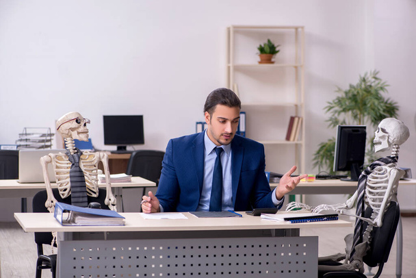 Fiatal férfi alkalmazott csontvázakkal az irodában - Fotó, kép