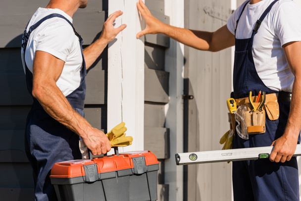 Cropped view of builders with toolbox and tool belt standing near facade of building outdoors  - Photo, Image