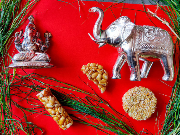 Ganesha / Vinaygar, Elefantenspielzeug und Erdnuss-Chikki umgeben von Gras. Vereinzelt auf rotem Hintergrund. Tamilische Tradition. Glückliche vinayagar chaturthi. - Foto, Bild