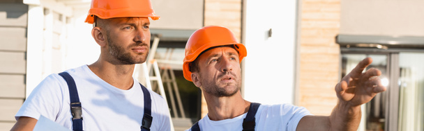 Panoramaaufnahme eines Bauarbeiters, der mit der Hand in die Nähe eines Kollegen im Freien zeigt  - Foto, Bild