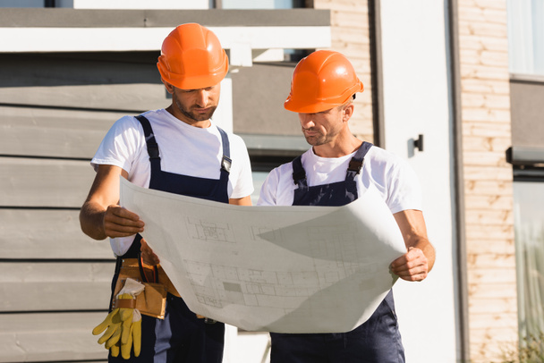 Bauarbeiter halten Bauplan fest, während sie nahe am Gebäude arbeiten  - Foto, Bild