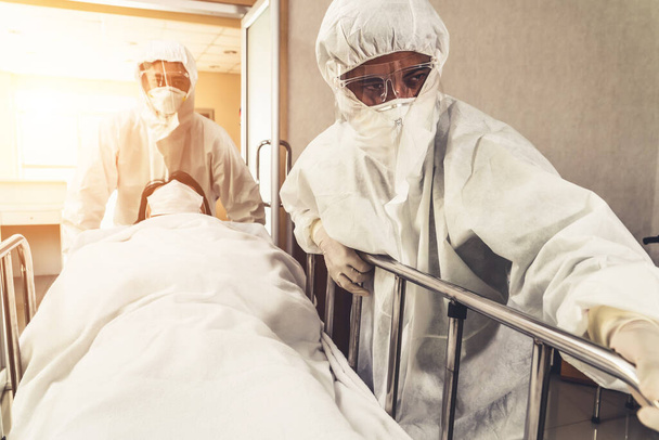Γιατρός έκτακτης ανάγκης και γιατρός μετακινούν ασθενή στα επείγοντα στο νοσοκομείο. Γιατρός φοράει προστατευτική στολή και μάσκα προσώπου στην έννοια του coronavirus και covid 19 προστασία και καραντίνα . - Φωτογραφία, εικόνα