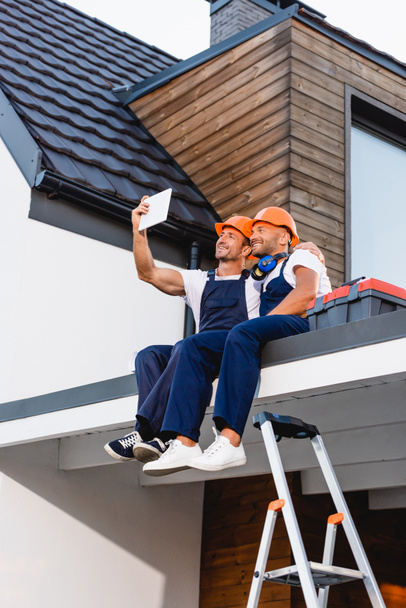 Builders taking selfie on digital tablet while sitting on roof of building  - Photo, Image
