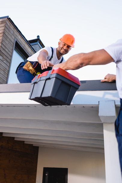 Foco seletivo do construtor dando caixa de ferramentas ao colega no telhado da casa  - Foto, Imagem