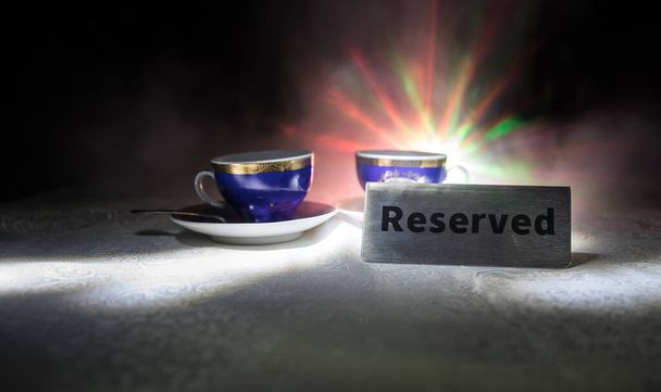 Reserved sign on the table. A tag of reservation placed on the wood table. Metal tag with reservation on dark. Reserved table in a restaurant. Creative concept with colorful lights. Selective focus - Photo, Image