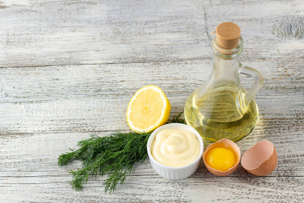 Salsa de mayonesa con limón, huevo, aceite y hierbas sobre fondo de madera blanca - Foto, Imagen