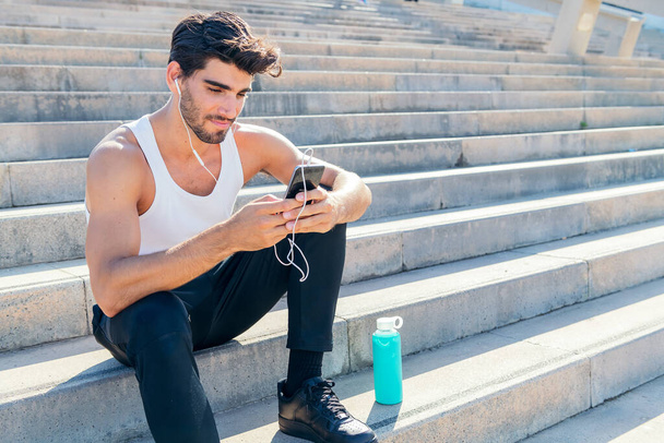 sportsman with earphone selects music on his phone to listen during his training, urban sport concept and healthy lifestyle, copy space for text - Foto, afbeelding
