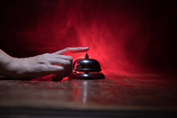 Κλήση καμπάνα υπηρεσίας σε ξύλινο τραπέζι με τονισμένα φώτα σε σκούρο φόντο. Hotel reception bell, Χέρι κλήσης σε καμπάνα υπηρεσίας, επιλεκτική εστίαση - Φωτογραφία, εικόνα