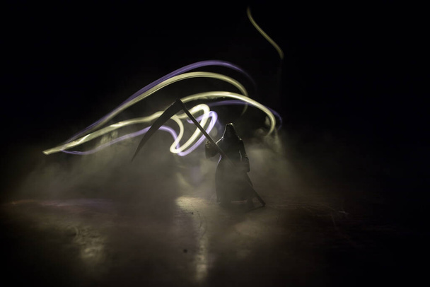 Death with a scythe on dark foggy toned background. Woman horror ghost holding reaper. Miniature artwork decoration. Halloween concept. Selective focus - Φωτογραφία, εικόνα