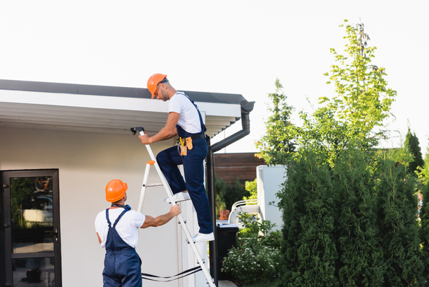 Bauarbeiter mit Leiter nahe Hausfassade und Hausdach in Stadtstraße  - Foto, Bild