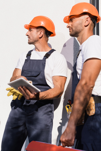Selective focus of handymen with digital tablet and toolbox standing near facade of building  - Photo, Image