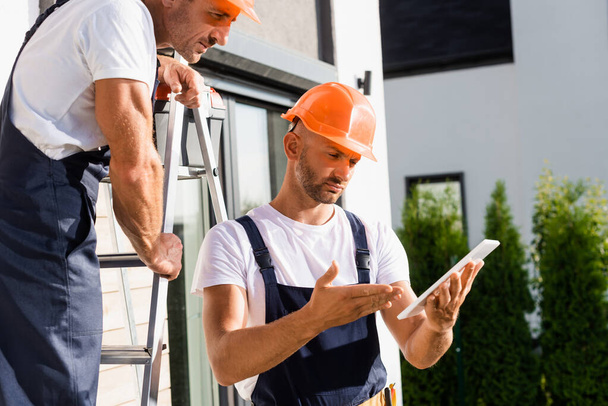 Вибіркове фокусування будівельника на драбині стоїть поруч з колегою вказуючи рукою на цифровий планшет поруч з будівлею  - Фото, зображення