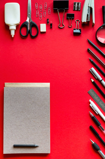 Notepad pennen en potloden op een rode achtergrond. Bovenaanzicht met kopieerruimte - Foto, afbeelding