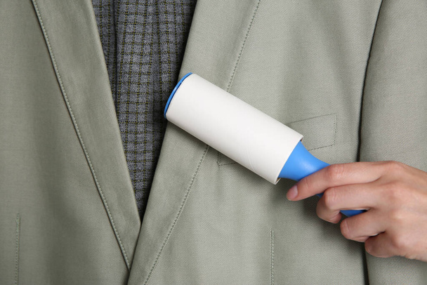 Woman cleaning light grey jacket with lint roller, closeup - Foto, imagen