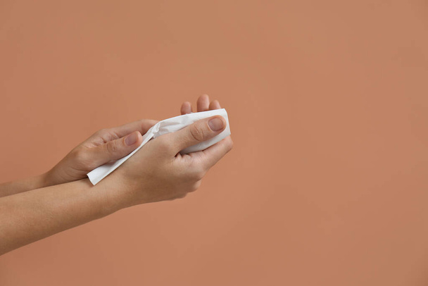 Woman cleaning hands with paper tissue on light brown background, closeup. Space for text - Fotografie, Obrázek