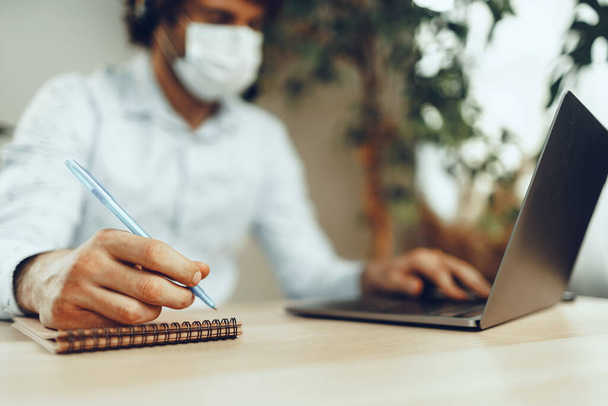Man in medical mask working from home while coronavirus quarantine - Foto, afbeelding