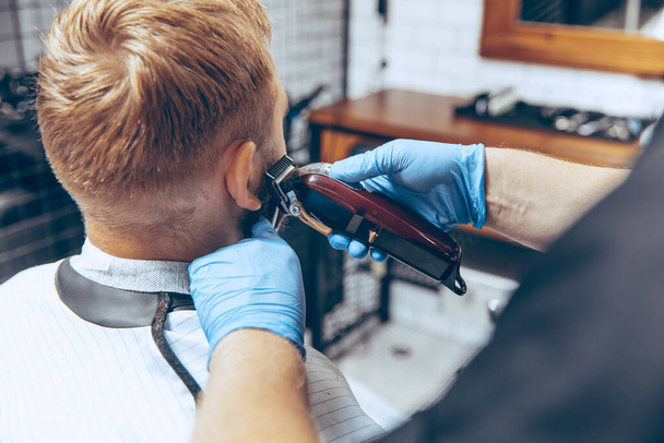 Man getting hair cut at the barbershop wearing mask during coronavirus pandemic - Foto, Imagen