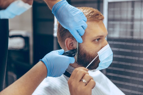 Мужчина стрижется в парикмахерской в маске во время пандемии коронавируса - Фото, изображение