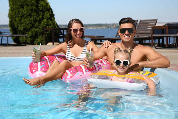 Happy family with inflatable rings and cocktails in outdoor swimming pool on sunny summer day - Photo, Image