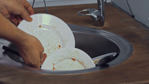 Vista ritagliata dell'uomo mettendo stoviglie nel lavandino della cucina  - Filmati, video