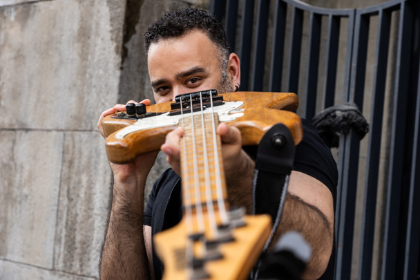 Handsome Male Person is Looking Through his Bass Guitar on Street. Playful Caucasian Young Person at Outdoor Event. - Photo, Image
