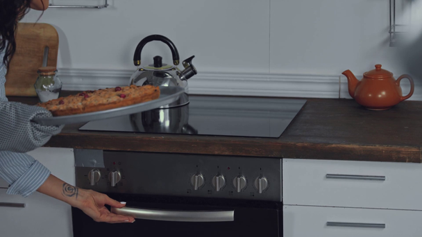 jonge vrouw in schort brengen taart uit oven in keuken  - Video