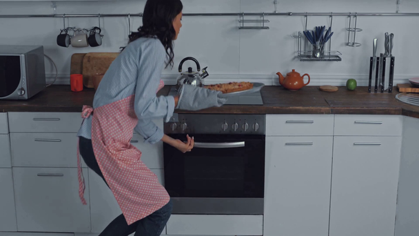 Женщина в фартуке берет и нюхает пирог из духовки на кухне  - Кадры, видео