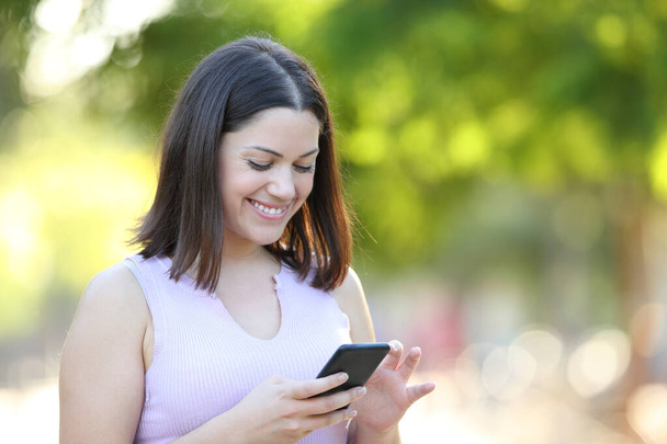 Happy woman walking in a park checking smart phone content - Foto, imagen
