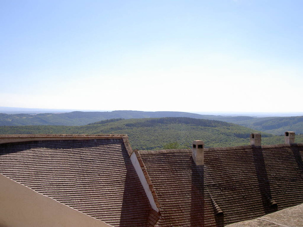 Vista sobre telhados antigos de casas na distância com colinas e florestas, fundo céu azul, imagem - Foto, Imagem