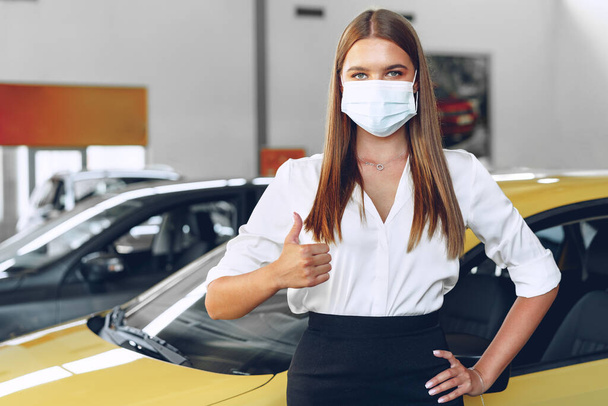 Woman car seller standing near new car wearing protective face mask - Фото, изображение