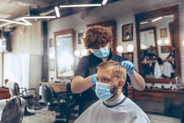 Un homme se fait couper les cheveux au salon de coiffure portant un masque pendant une pandémie de coronavirus - Photo, image