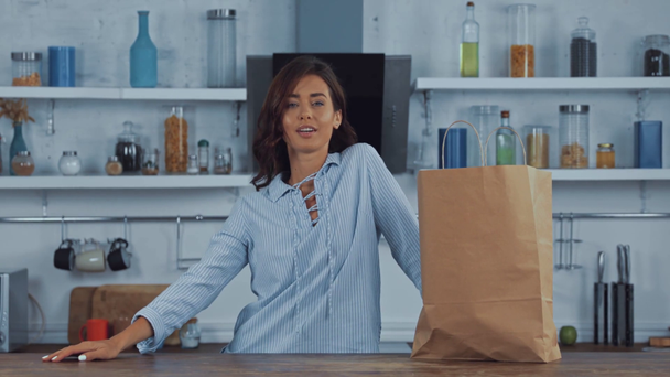 Νεαρή γυναίκα βάζει χάρτινη σακούλα στο τραπέζι της κουζίνας  - Πλάνα, βίντεο