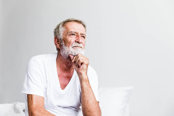 Egy nyugdíjas férfi portréja, aki egyedül ül és gondolkodik az ágyán az otthonában. - Fotó, kép