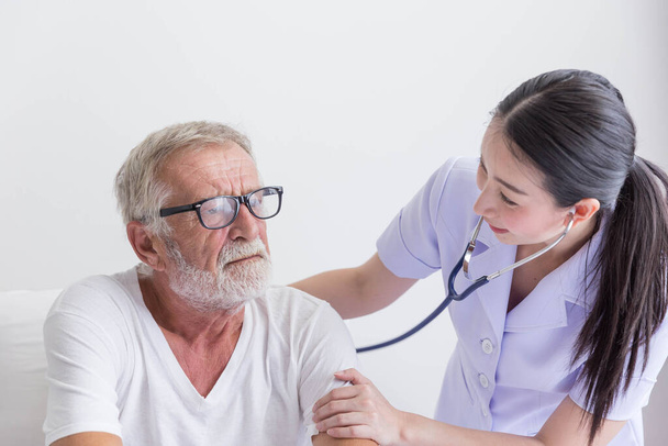 Pielęgniarka ze stetoskopem odwiedza seniora i sprawdza jego bicie serca na łóżku - Zdjęcie, obraz