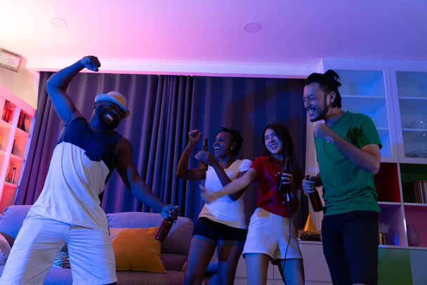 Friends laughing in sofa at home party under colorful light with drink and snack - Fotó, kép