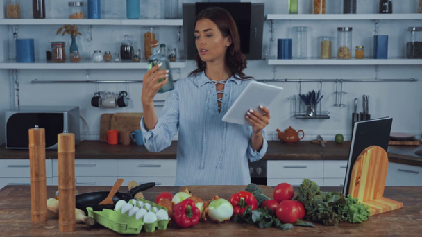 Mutfakta yemek pişirirken çiğ sebzelerin yanında dijital tablet kullanan kadın.  - Video, Çekim