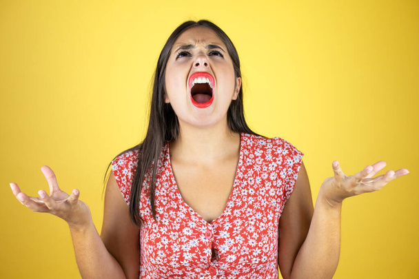 Jonge mooie vrouw over geïsoleerde gele achtergrond gek en gek schreeuwen en schreeuwen met agressieve uitdrukking en armen opgeheven - Foto, afbeelding