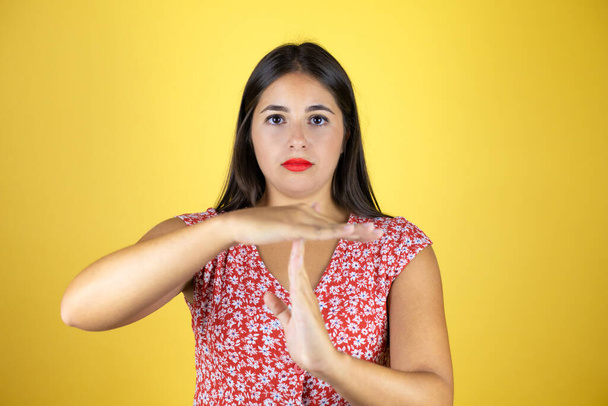 Mladá krásná žena přes izolované žluté pozadí odpykávající si čas gesto s rukama, frustrovaný a vážný obličej - Fotografie, Obrázek