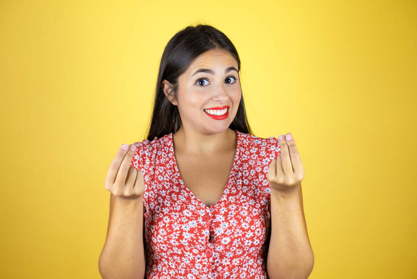 Young beautiful woman over isolated yellow background doing money gesture with hands, asking for salary payment, millionaire business - Foto, Bild