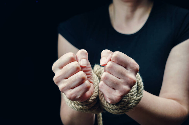 Handen van een slachtoffer vrouw vastgebonden met ruw touw op de zwarte achtergrond. Stop met geweld te misbruiken - Foto, afbeelding