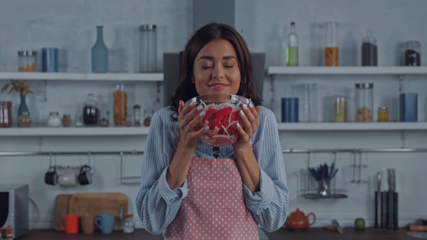 Женщина в фартуке показывает миску свежего салата на кухне - Кадры, видео