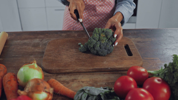 Καλλιεργημένη άποψη της γυναίκας κοπής μπρόκολο κοντά ώριμα λαχανικά στην κουζίνα  - Πλάνα, βίντεο