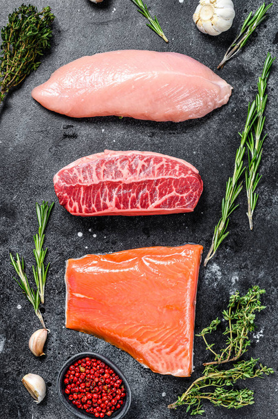 Raw steaks. Beef top blade, salmon fillet and Turkey breast. Organic fish, poultry and beef meat. Black background. Top view. - Photo, Image