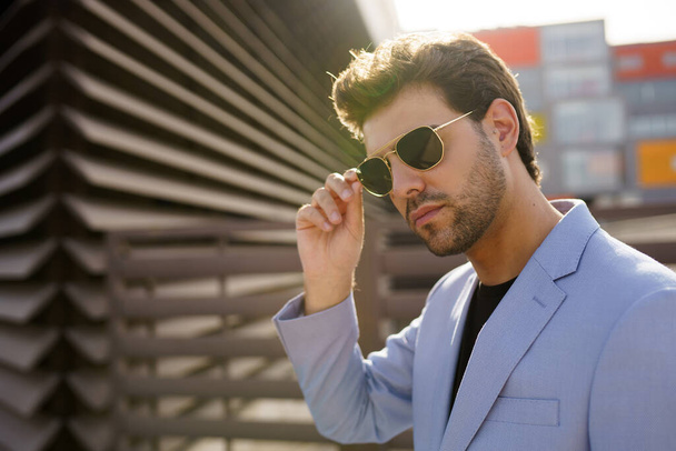 Jonge knappe man draagt een zonnebril in stedelijke achtergrond - Foto, afbeelding