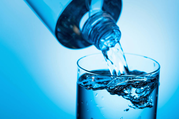 Víz öntése egy palackból üvegbe, kék alapon. Fénymásolási hely. - Fotó, kép
