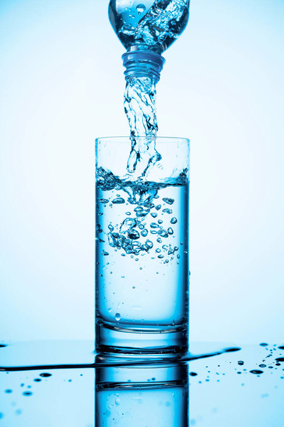 Verser l'eau d'une bouteille dans un verre sur un fond bleu. Espace de copie. - Photo, image