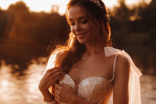 An elegant bride in a white dress enjoys nature at sunset.Model in a wedding dress in nature in the Park.Belarus. - Fotoğraf, Görsel