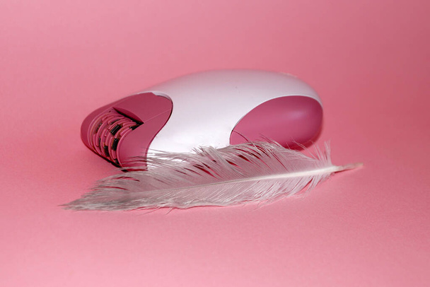 electric handheld epilator and feather on pink background close-up - 写真・画像