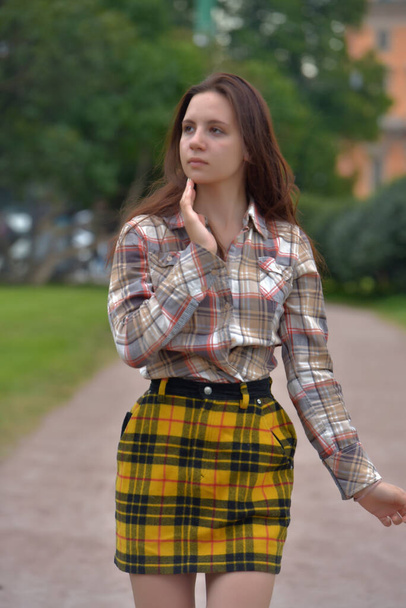 beautiful slender brunette girl in a plaid skirt in the summer in the park - Fotoğraf, Görsel