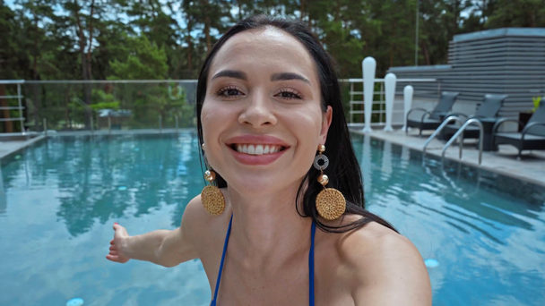 morena mujer saludando de la mano y mostrando gesto acogedor cerca de la piscina  - Metraje, vídeo